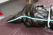 Jill tied, gagged and hooded on bed wearing a shiny black downjacket and shiny blue rain pants (Pics)