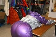 Jill tied and gagged on a table wearing a shiny purple/silver PVC sauna suit (Pics)