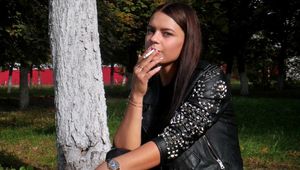Pretty faced Asya is smoking a cigarette outdoors
