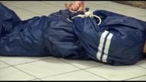 Jill tied and gagged on the floor in an old cellar wearing a shiny blue PVC sauna suit (Video)
