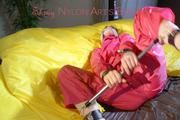 Lucy tied and gagged with a bar on a bed wearing a sexy pink shiny nylon rain pants and a rain jacket (Pics)