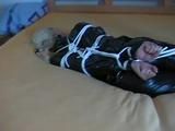 Blond-haired maid tied and gagged on bed wearing a shiny black PVC sauna suit (Video)