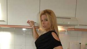 Pierced MILF Nina poses in a black dress, stockings and heels in the kitchen