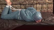 Mara tied, gagged and hooded on bed in a cellar wearing a shiny blue/grey downwear (Video)