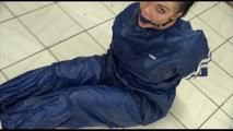 Jill tied and gagged on the floor in an old cellar wearing a shiny blue PVC sauna suit (Video)