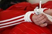 Jill tied and gagged lying on a sofa wearing a sexy shiny red adidas shorts and a red rain jacket (Pics)