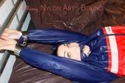 Jill tied and gagged on bed with cuffs and chains wearing a sexy red shiny nylon shorts and a blue shiny nylon rain jacket (Pics)