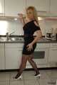 Pierced MILF Nina poses in a black dress, stockings and heels in the kitchen