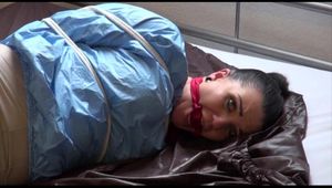 Jill tied and gagged on bed wearing a blue/offwhite shiny PVC suit combination (Video)