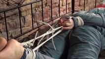 Mara tied, gagged and hooded on bed in a cellar wearing a shiny blue/grey downwear (Video)