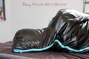 Jill tied, gagged and hooded on bed wearing a shiny black downjacket and shiny blue rain pants (Pics)