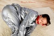 Alina tied and gagged in a shiny silver PVC saunasuit
