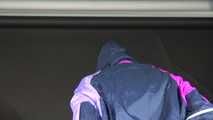 Watching Pia wearing a blue/purple/pink shiny nylon rain suit folding clothes and tidying up the studio (Video)