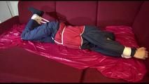 Lucy tied and gagged with ropes and a cloth gag on a sofa wearing a blue/red rainwear combination (Video)