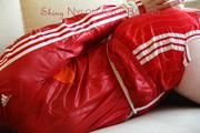 Jill tied and gagged lying on a sofa wearing a sexy shiny red adidas shorts and a red rain jacket (Pics)
