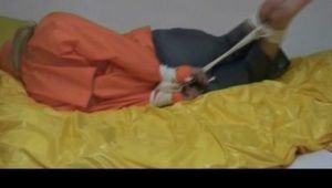 Samantha tied and gagged in bed wearing an orange/grey shiny nylon rainwear combination (Video)