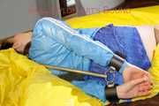 Lucy tied and gagged in a shiny nylon bed with on a bar behind her back and with a cloth gag wearing a blue shiny nylon shorts and a lightblue rain jacket (Pics)