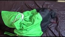 Jill tied and gagged on bed wearing a blue/black shiny rainwear combination with an raincape over it (Video)