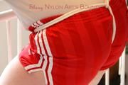 Jill tied and gagged standing on a stairway wearing a sexy red adidas shiny nylon shorts and a top (Pics)