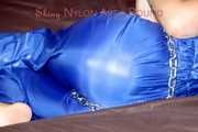 PIA tied and gagged with a pillory on a sofa wearing a sexy blue really shiny nylon rain bib overall (Pics)