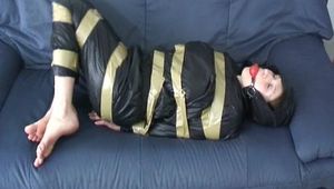 Katharina tied and gagged with tape on a sofa wearing a shiny black nylon rainsuit (Video)