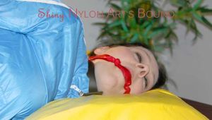 Lucy tied and gagged in a shiny nylon bed with on a bar behind her back and with a cloth gag wearing a blue shiny nylon shorts and a lightblue rain jacket (Pics)