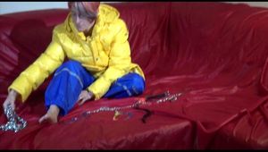 Sonja wearing a blue rain pants and a yellow PAMY down jacket while bonding herself an the sofa (Video)