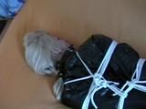 Blond-haired maid tied and gagged on bed wearing a shiny black PVC sauna suit (Video)