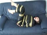 Katharina tied and gagged with tape on a sofa wearing a shiny black nylon rainsuit (Video)