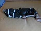 Blond-haired maid tied and gagged on bed wearing a shiny black PVC sauna suit (Video)