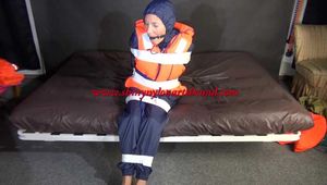 Sexy Sandra being tied and gagged with tape on a bed wearing blue rainwear and a lifevest (Video)