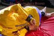Sonja tied and gagged on bed with cuffs and neckband wearing a sexy blue shiny nylon shorts and a yellow rain jacket (Pics)