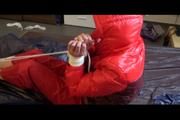 Pia tied and gagged on bed wearing a shiny red rain pants and a shiny red/purple down jacket (Video)