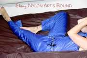 PIA tied and gagged with a pillory on a sofa wearing a sexy blue really shiny nylon rain bib overall (Pics)