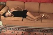 Video : Hogtied asian girl Ann is struggling on the couch in her sexy black dress.